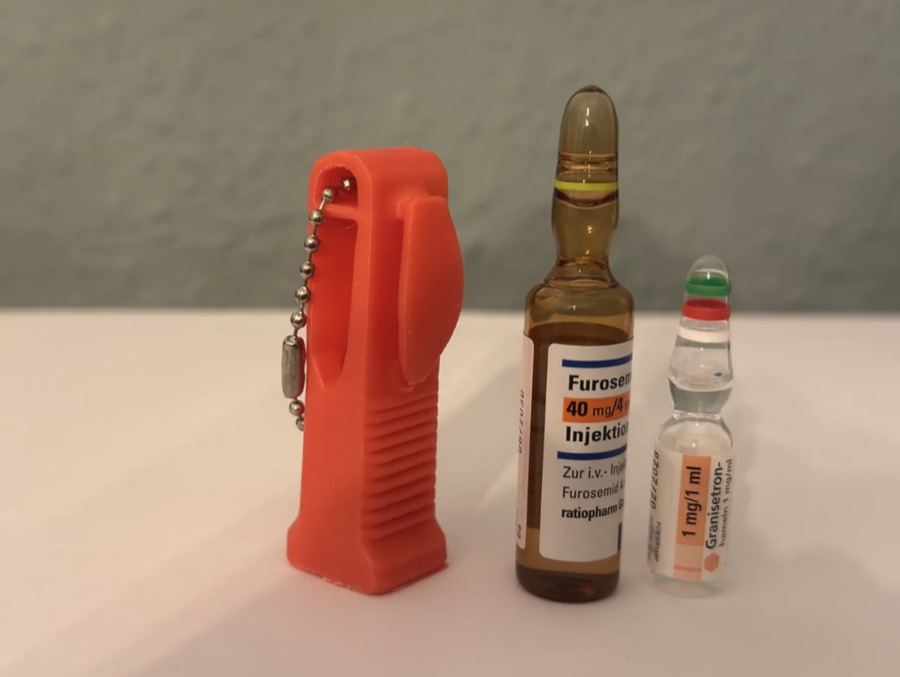 Abreampollas naranjo con clip y cadena de llavero junto a dos ampollas de vidrio