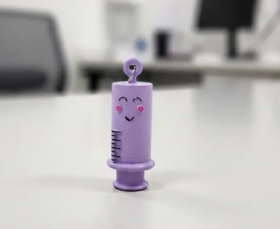Abreampollas lila con forma de jeringa sonriente y argolla para llavero