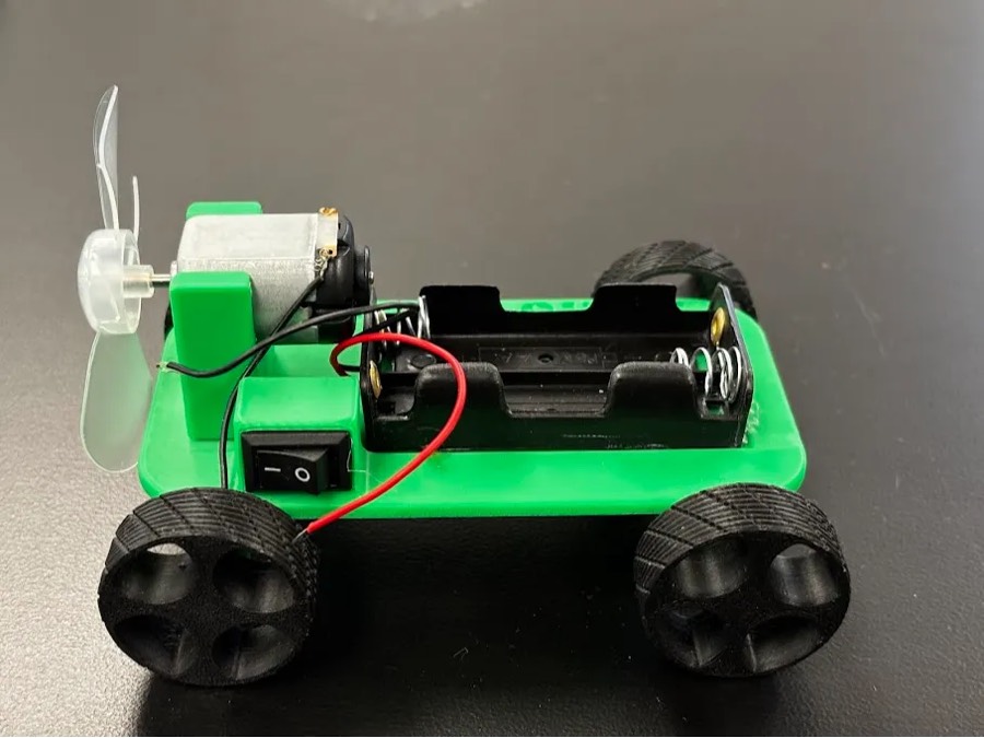 Carrito verde impreso en 3D con hélice, motor, interruptor y portapilas conectados con cables