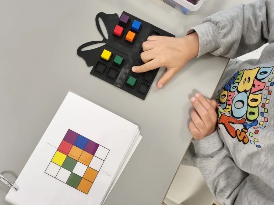 Niño armando un patrón de cubos de colores en un tablero siguiendo una tarjeta modelo