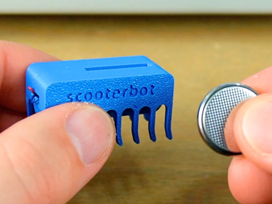 Mini robot azul con patas y una pila de botón en la otra mano